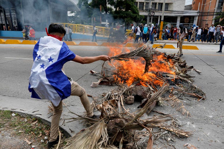 Un manifestante que usa la bandera hondureña como capa arroja madera al fuego durante una protesta en Tegucigalpa, Honduras, el martes 6 de agosto de 2019. Un manifestante que usa la bandera hondureña como capa arroja madera al fuego durante una protesta en Tegucigalpa, Honduras, el martes 6 de agosto de 2019.