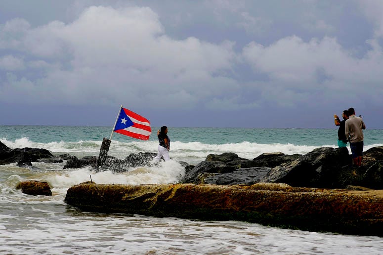 Una mujer posa para una fotografía con el mar y una bandera de Puerto Rico de fondo tras el paso de la tormenta tropical Dorian por la isla, en San Juan, Puerto Rico, el 28 de agosto de 2019. Una mujer posa para una fotografía con el mar y una bandera de Puerto Rico de fondo tras el paso de la tormenta tropical Dorian por la isla, en San Juan, Puerto Rico, el 28 de agosto de 2019.