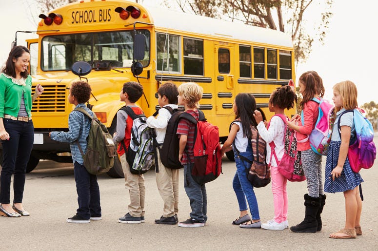 Teacher and a group of elementary school kids at a bus stop School Bus