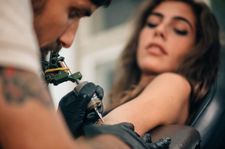 Tattoo artist creating a tattoo on a girl's arm. Focus on tattoo machine Tattoo artist creating a tattoo on a girl's arm. Focus on tattoo machine