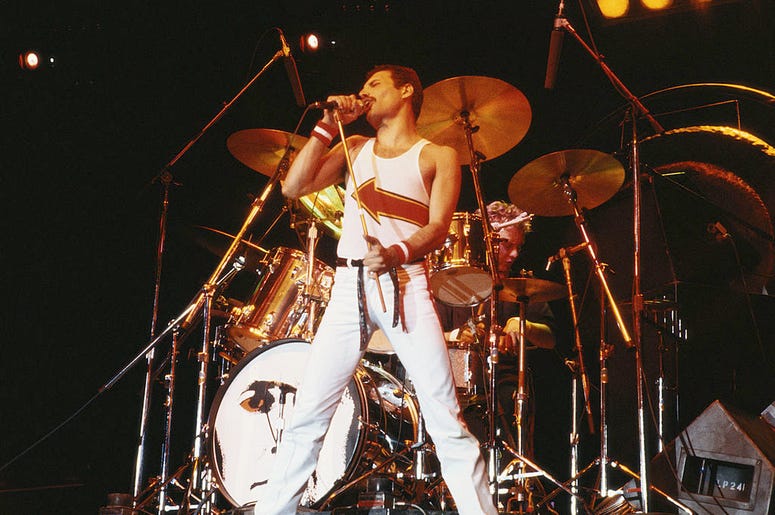 Freddie Mercury (1946-1991), singer with Queen, standing in front of a drumkit as he sings into a microphone on stage during a live concert performance by the band at the National Bowl in Milton Keynes, England, United Kingdom, on 5 June 1982. Freddie Mercury (1946-1991), singer with Queen, standing in front of a drumkit as he sings into a microphone on stage during a live concert performance by the band at the National Bowl in Milton Keynes, England, United Kingdom, on 5 June 1982.