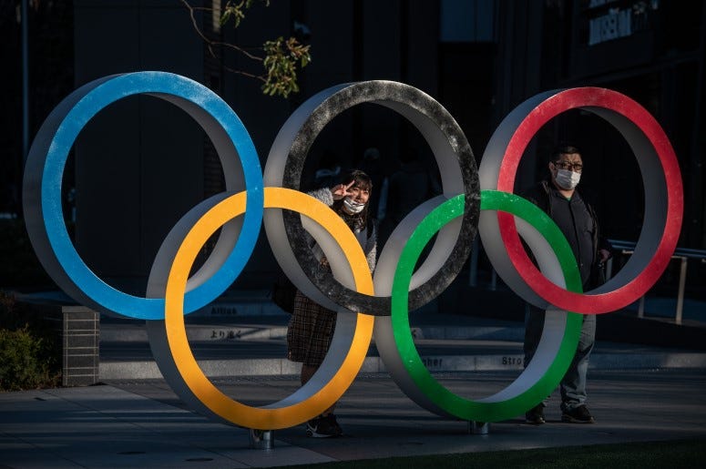 People wearing face masks pose for photographs next to Olympic Rings in Tokyo, Japan. The 2020 Olympic Games are postponed.
