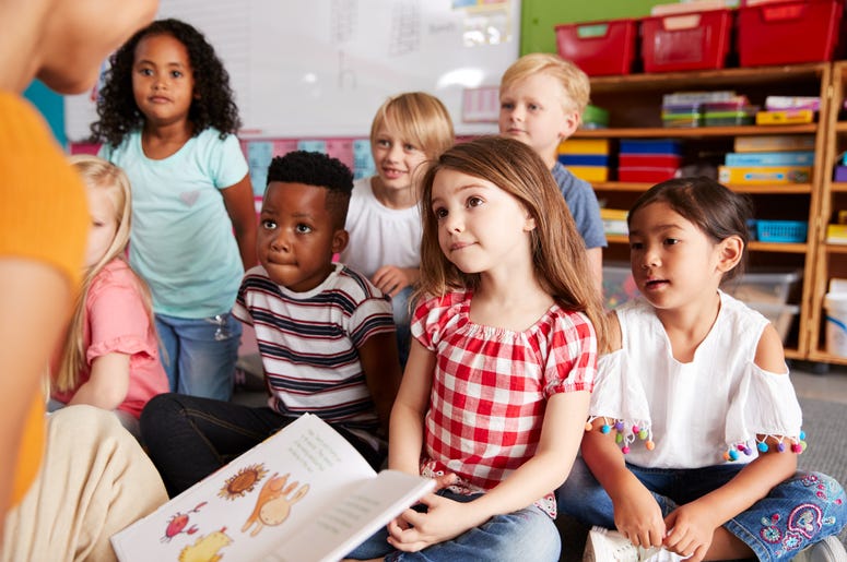 A proposed bill would add funding to Maryland school systems. Young children gather together in front of a teacher, who is reading a book.