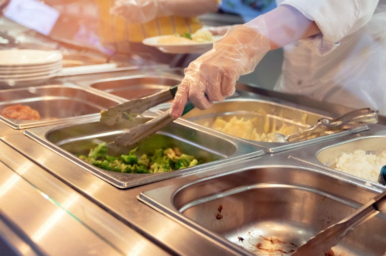 Photo courtesy of Getty Stock Images Chef standing behind full lunch service station with assortment of food in trays.