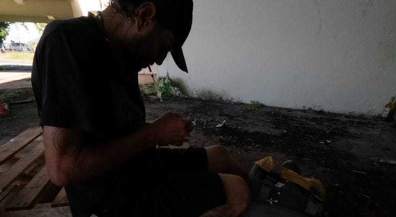A heroin addict prepares to shoot up outside