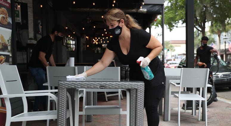 Maria Iraola wipes down the sidewalk tables of the Argentino Las Olas restaurant as it prepares to open to customers in Fort Lauderdale, Florida.