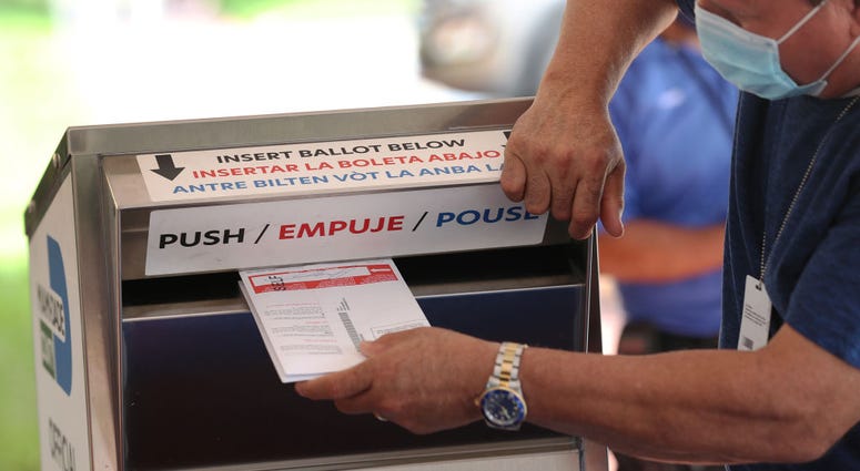 A poll workers places Vote-by Mail ballots into a ballot box set up at the Miami-Dade Election Department headquarters on October 14, 2020 in Doral, Florida.