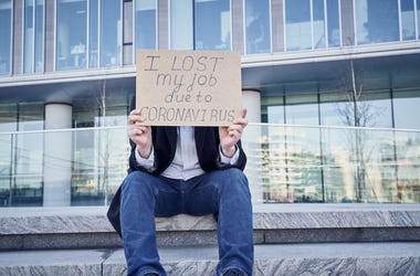 A man holds sign "I lost my job because of coronavirus." as he sits Male sitting on stairs of building at his former place of work in the business center. A man holds sign "I lost my job because of coronavirus." as he sits Male sitting on stairs of building at his former place of work in the business center.
