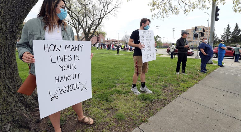KANSAS CITY, MISSOURI - APRIL 20: Counter-protesters McKinley Callin and Alec Overmann hold signs during a protest demanding that businesses be allowed to open up, and people allowed to go back to work. (Photo by Jamie Squire/Getty Images) Coronavirus