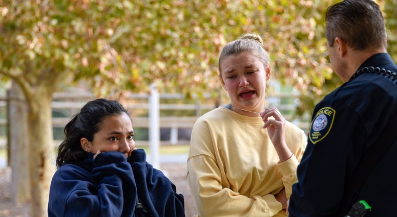 Two Saugus High students talk to a police officer at a reunification point after a shooting at Saugus high school in Santa Clarita, California. Family members were reunited with students at Grand Park located near the school.